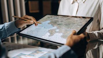 A business analyst manipulating a floating 3D holographic map zooming in to highlight specific regions while noting strategic sales data on a digital tablet.. photo