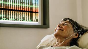A senior smiling softly with electrodes visible on their scalp as a colorful LED light display pulses rhythmically indicating progress in relaxation techniques.. photo