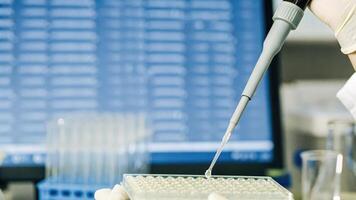 A researcher pipetting a clear solution into a multiwell plate surrounded by various lab equipment as a digital display in the background shows realtime gene expression data.. photo