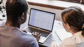 The couple sits side by side at a workstation intently focused on a laptop screen showcasing advanced genetic data analysis their expressions a mix of curiosity and concentration.. photo