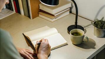 A focused individual writing in a leatherbound journal illuminated by a warm desk lamp with a steaming cup of herbal tea beside them capturing a moment of introspective reflection.. photo