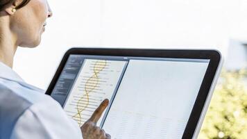A midshot of a backlit DNA hologram hovering above a touchscreen interface where a biohacker analyzes genetic data with swift finger movements signifying tingedge research in. photo
