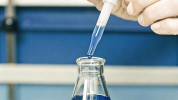 A closeup shot of a scientists hands carefully pipetting a bright blue dye into a flask showcasing the precise technique required in cell culture techniques.. photo