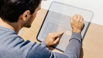 A gentleman with a thoughtful expression engages with a holographic screen that features a visual comparison of his pressure readings over the months highlighting improvements.. photo