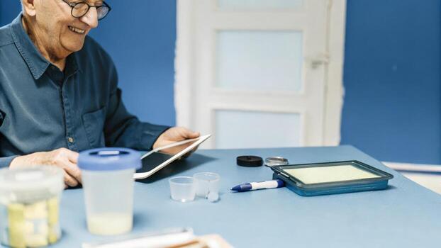 An elderly man smiles as he inputs data into a healthtracking app on a tablet surrounded by various tools like a pedometer measuring cups and a insulin pen for managing his. photo