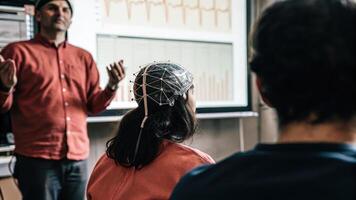 A researcher demonstrating a neurofeedback exercise to a small group with electrodes p on a participants head visually portraying the intersection of technology and human. photo