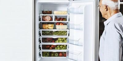 An elderly man standing in front of an open refrigerator packed with fresh produce and containers of preportioned meals showcasing an organized and healthfocused approach to daily. photo