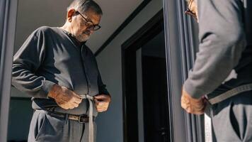 A senior man stands in front of a fulllength mirror adjusting smart body measuring ss around his waist with a look of determination as he prepares for his muscle mass assessment.. photo
