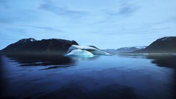 Majestic iceberg drifting in calm waters surrounded by mountains at dusk video