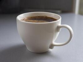 White mug filled with steaming hot coffee resting on a gray table, radiating a cozy and inviting atmosphere perfect for enjoying a morning beverage or relaxing break photo