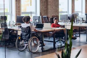 Business colleagues work within a modern startup coworking office, with one of them, an African America in a wheelchair, actively engaging with computers and laptops to collaboratively address various photo