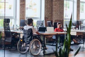 Business colleagues work within a modern startup coworking office, with one of them, an African America in a wheelchair, actively engaging with computers and laptops to collaboratively address various photo