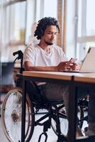 An African American businessman in a wheelchair takes a work break, using his smartphone while seated in a modern business startup coworking center, reflecting both inclusion and technology photo