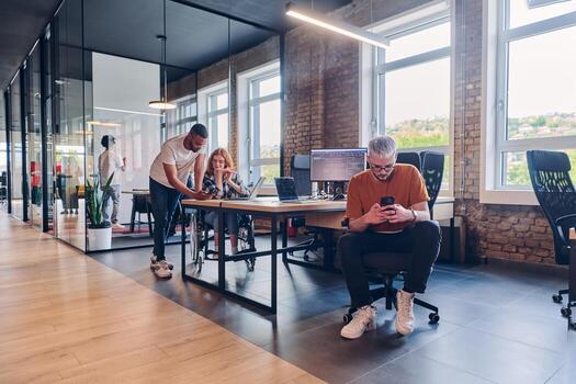 A diverse group of business professionals collaborates in a modern startup coworking center, utilizing a mix of paper-based and technological tools such as mobile phones and computers to collectively photo