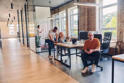 A diverse group of business professionals collaborates in a modern startup coworking center, utilizing a mix of paper-based and technological tools such as mobile phones and computers to collectively photo