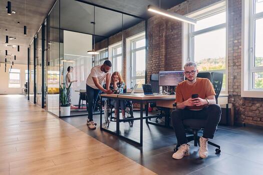 A diverse group of business professionals collaborates in a modern startup coworking center, utilizing a mix of paper-based and technological tools such as mobile phones and computers to collectively photo
