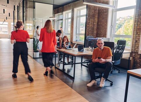 A diverse group of business professionals collaborates in a modern startup coworking center, utilizing a mix of paper-based and technological tools such as mobile phones and computers to collectively photo