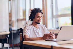 An African American businessman in a wheelchair takes a work break, using his smartphone while seated in a modern business startup coworking center, reflecting both inclusion and technology photo