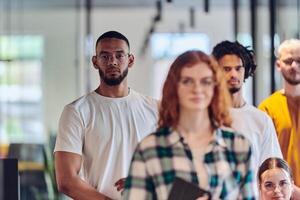 A diverse group of business people walking a corridor in the glass-enclosed office of a modern startup, including a person in a wheelchair and a woman wearing a hijab, showing a dynamic mix of photo