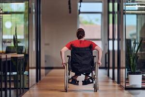 A modern young businesswoman in a wheelchair is surrounded by an inclusive workspace with glass-walled offices, embodying determination and innovation in the business world photo