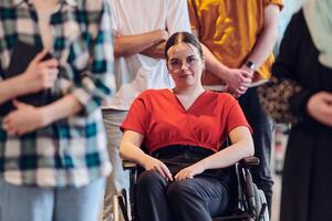 A diverse group of business people walking a corridor in the glass-enclosed office of a modern startup, including a person in a wheelchair and a woman wearing a hijab, showing a dynamic mix of photo