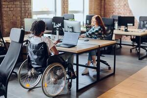 Business colleagues work within a modern startup coworking office, with one of them, an African America in a wheelchair, actively engaging with computers and laptops to collaboratively address various photo