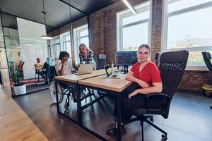 A young business group, including an African American businessman in a wheelchair, collaborates within a modern glass office, actively engaged around a computer and laptop, collectively solving photo