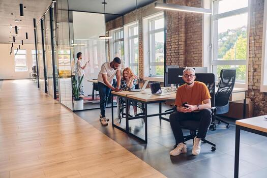 A diverse group of business professionals collaborates in a modern startup coworking center, utilizing a mix of paper-based and technological tools such as mobile phones and computers to collectively photo
