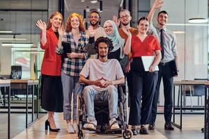 A diverse group of young business people congregates within a modern startup's glass-enclosed office, featuring inclusivity with a person in a wheelchair, an African American young man , and a hijab photo