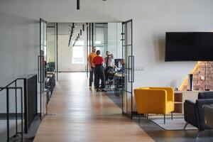 A business group, including an African American businessman in a wheelchair, collaborates within a modern glass office, actively engaged around a computer and laptop, collectively solving diverse photo