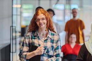 A diverse group of business people walking a corridor in the glass-enclosed office of a modern startup, including a person in a wheelchair and a woman wearing a hijab, showing a dynamic mix of photo