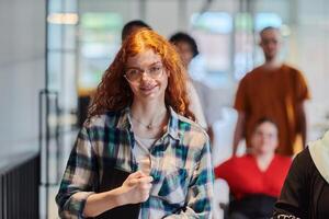 A diverse group of business people walking a corridor in the glass-enclosed office of a modern startup, including a person in a wheelchair and a woman wearing a hijab, showing a dynamic mix of photo