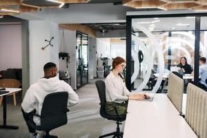 Two colleagues collaborating in a modern office while discussing a project using a tablet and laptop. photo