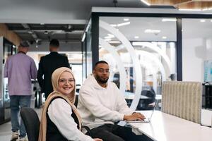 In a modern office setting, an African American businessman and his Muslim colleague, wearing a hijab, engage in collaborative discussions, tackling various business tasks and solving problems photo