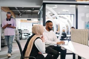 In a modern office setting, an African American businessman and his Muslim colleague, wearing a hijab, engage in collaborative discussions, tackling various business tasks and solving problems photo
