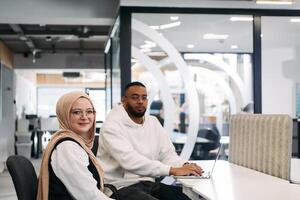 In a modern office setting, an African American businessman and his Muslim colleague, wearing a hijab, engage in collaborative discussions, tackling various business tasks and solving problems photo