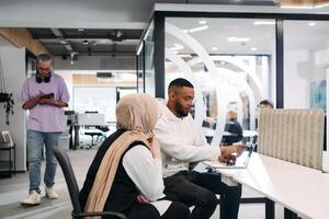 In a modern office setting, an African American businessman and his Muslim colleague, wearing a hijab, engage in collaborative discussions, tackling various business tasks and solving problems photo