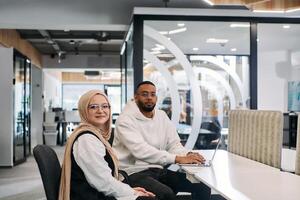 In a modern office setting, an African American businessman and his Muslim colleague, wearing a hijab, engage in collaborative discussions, tackling various business tasks and solving problems photo