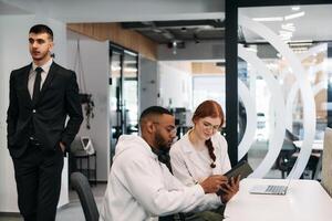 Two colleagues collaborating in a modern office while discussing a project using a tablet and laptop. photo