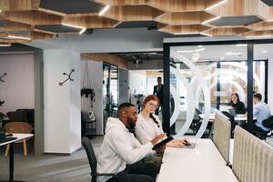 Two colleagues collaborating in a modern office while discussing a project using a tablet and laptop. photo