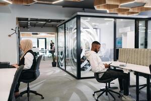 In a modern office setting, an African American businessman and his Muslim colleague, wearing a hijab, engage in collaborative discussions, tackling various business tasks and solving problems photo