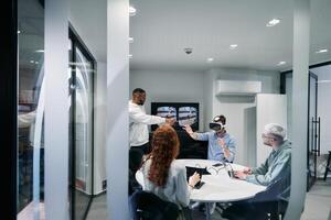 A diverse group of businessmen collaborates and tests a new virtual reality technology, wearing virtual glasses, showcasing innovation and creativity in their futuristic workspace photo
