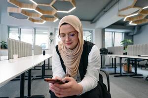 A businesswoman in a hijab using a smartphone in a modern office, epitomizing a successful and empowered professional in today's tech-savvy world photo