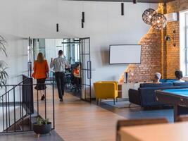 A business group, including an African American businessman in a wheelchair, collaborates within a modern glass office, actively engaged around a computer and laptop, collectively solving diverse photo