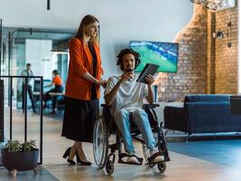 African-American businessman in a wheelchair engages in a collaborative discussion, using a tablet, with his business colleague, exemplifying the seamless integration of adaptive technology and photo
