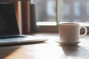 Warm coffee beside a laptop in a cozy workspace during morning light photo