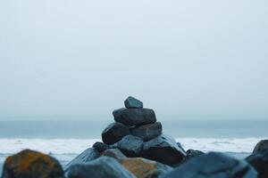Stacked stones on a misty beach with gentle waves in the background during a serene overcast day photo