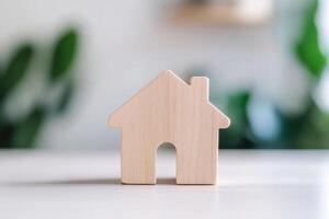 Simple wooden house figure on a table with greenery in the background photo