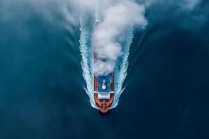 Large cargo ship navigates through ocean waters creating waves and mist during daylight photo