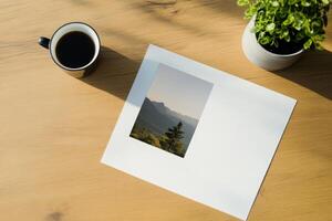 Coffee and a landscape print on a wooden table with a green plant in the background during a calm morning photo
